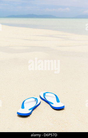 Blue flip flop su un'idilliaca spiaggia di sabbia bianca, molto leggera profondità di campo a. Foto Stock
