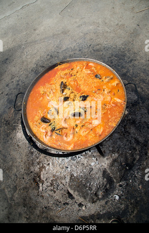 La paella spagnola per la cottura in una padella in tizzi caldi Foto Stock