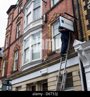 Lavoro in altezza: un operaio in piedi su una scaletta di sostituzione riparazione il segno al di fuori di un ramo di Lloyds TSB Bank, Regno Unito Foto Stock