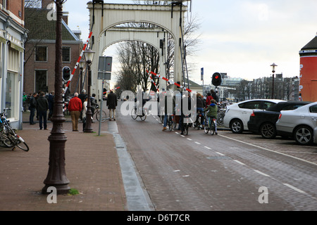 I ciclisti e i pedoni in attesa in corrispondenza di una luce di colore rosso e la barriera mentre un ponte girevole di Amsterdam si chiude Foto Stock