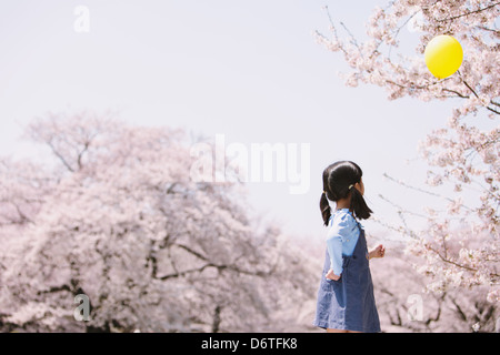 Ragazza giovane con palloncino e ciliegi in background Foto Stock