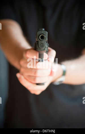 Giovane uomo puntando alla fotocamera con una pistola. Il fuoco selettivo sulla pistola. Foto Stock