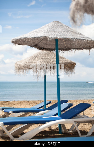 Prendere il sole sedie a sdraio e ombrelloni di paglia sulla spiaggia. Foto Stock