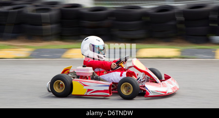 Giovane ragazzo asiatico in un rosso e bianco gara tuta e casco in un go kart Foto Stock