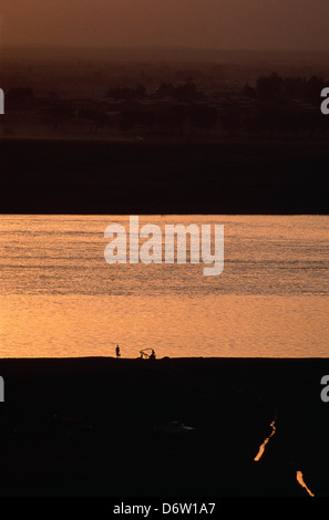 Il fiume Nilo a Khartoum durante il tramonto con un coltivatore solitario che porta un secchio di acqua dal Nilo per la sua azienda Foto Stock