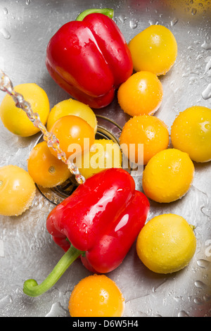 Il lavaggio di rosso e di giallo di frutta e verdura in il lavandino della cucina. Foto Stock