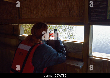 Giovane donna che indossa la canoa PFD in bird-watching nascondi scatta una fotografia del Cockshoot Broad, Norfolk sul suo dispositivo Blackberry Foto Stock
