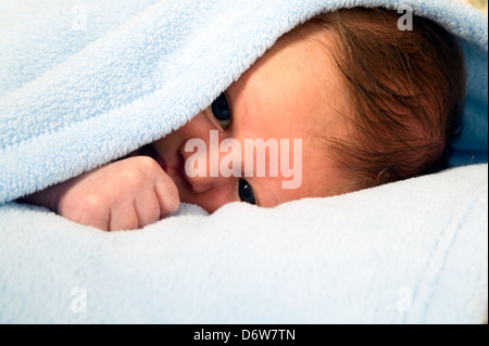 Bella bianca baby boy con grandi occhi è giacente sotto la coperta Foto Stock