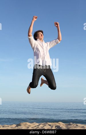 Boy jumping happy sulla spiaggia con il mare e con un cielo blu in background Foto Stock