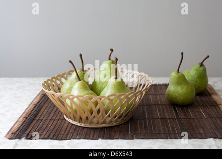 Sei pere verde in un tessuto piatto di rattan e su un tappetino di bambù con un leggero tovaglia modellato Foto Stock