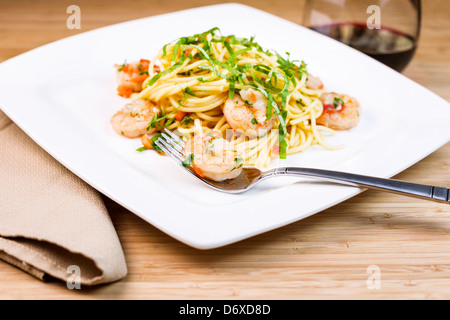 Closeup foto orizzontale di un piatto di pasta con focus su gamberi grandi in acciaio inossidabile forcella, basilico, panno assorbente, e vino rosso Foto Stock