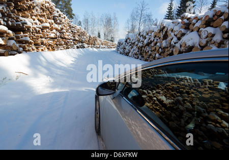 Auto ( Toyota Avensis ) sul disboscamento di inventario delle strade mucchi di tronchi in attesa di trasporto, Finlandia Foto Stock