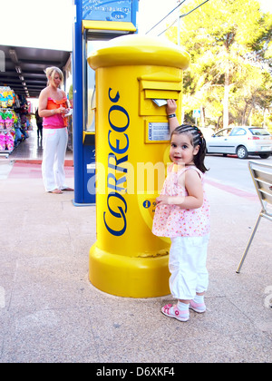 Una giovane ragazza posti una lettera in un giallo spagnolo casella postale Foto Stock