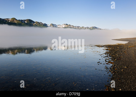 Vista sulle montagne con le nuvole e riflessa in acqua da una baia Foto Stock