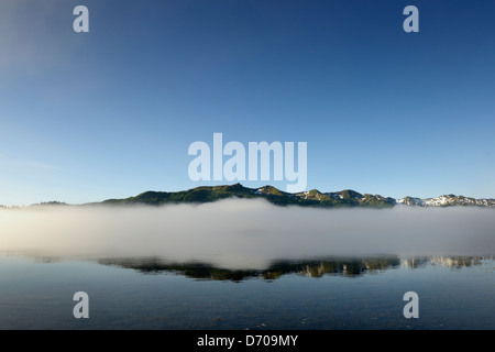 Vista sulle montagne con le nuvole e riflessa in acqua da una baia Foto Stock