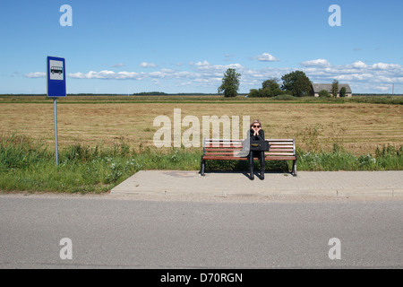 Lonely donna in attesa di un autobus in zona rurale Foto Stock