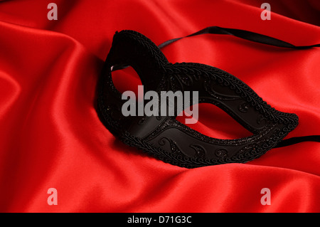Maschera nera su raso rosso sfondo. Foto Stock