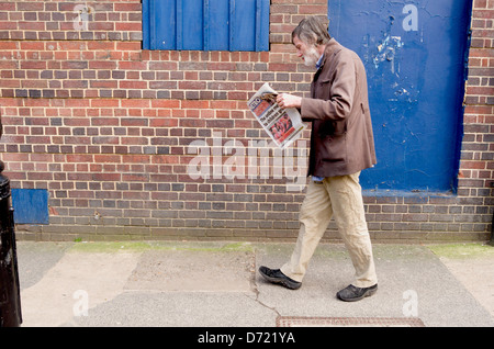 Uomo che cammina mentre leggendo un giornale. Foto Stock