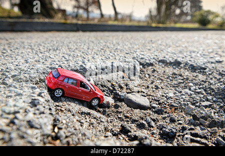 Auto in miniatura nel foro di sfiato sulla strada, simbolico photo street danni Foto Stock