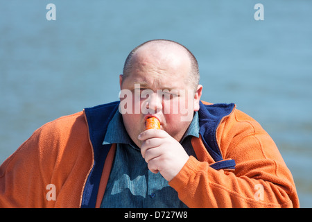 Fat man di mangiare una carota, su uno sfondo di acqua Foto Stock