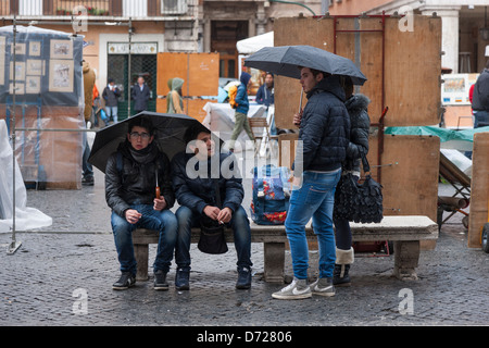 La gente si ripara dalla pioggia sotto gli ombrelloni a buon mercato in Piazza Navona, Roma, Italia Foto Stock