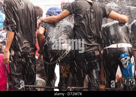 Giovani uomini salire sulla cima di veicoli in movimento alla danza e ottenere alloggiata come essi passano per le piattaforme di acqua durante la celebrazione Thingyan. Foto Stock