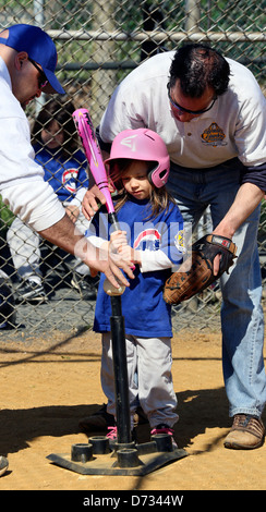 Una bambina t-ball tee ball giocatore di baseball con due allenatori aiutandola withe il suo atteggiamento di ovatta. Foto Stock