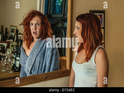 Ragazza vestita con intelligenza che guarda nello specchio e che vede il suo unkempt lato come un riflesso Foto Stock