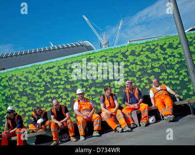 Sette dipendenti indossando orange alta visibilità saftey abbigliamento prendendo una pausa sul Kings Boulevard, Kings Cross, London Foto Stock