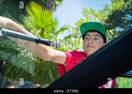 Un adolescente di sesso maschile in un cappello da baseball usa una spatola di asciugare una finestra di un auto presso una scuola di fund raising car wash. Foto Stock