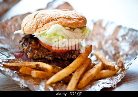 Inquadratura ravvicinata di un burger con doppia polpetta di carne di manzo, pomodori e lattuga. Servita con alcuni cajun patate fritte. Foto Stock