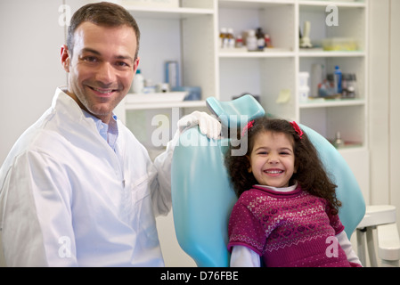 Medico durante la visita del bambino femmina in dental clinic, il Ritratto di giovane bambina guardando la fotocamera e sorridente Foto Stock