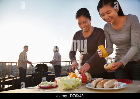 Madre e figlia la preparazione di hot dog per barbeque, padre e figlio di preparare le salsicce sul barbecue Foto Stock