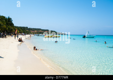 I turisti a languire su una soleggiata spiaggia tropicale mentre è in vacanza nell'Isola di Roatan, Honduras. Foto Stock