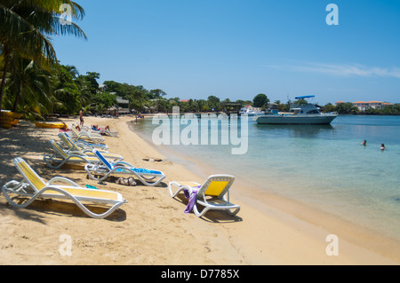 I turisti a languire su una soleggiata spiaggia tropicale mentre è in vacanza nell'Isola di Roatan, Honduras. Foto Stock