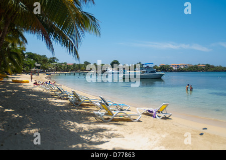 I turisti a languire su una soleggiata spiaggia tropicale mentre è in vacanza nell'Isola di Roatan, Honduras. Foto Stock
