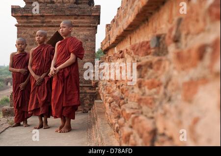 Tre giovani monaci buddisti sono in piedi accanto a un muro di mattoni di fronte ad un campo di Pagoda a Bagan, Myanmar, il 01.04.2013. Foto: Sebastian Kahnert Foto Stock