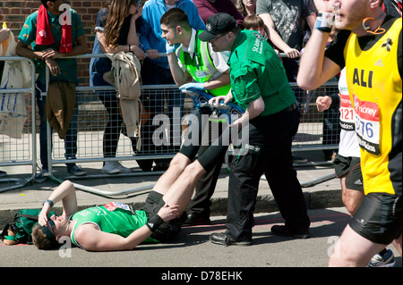 I membri di St Johns Ambulance trattando un maschio di runner per i crampi, per strada, durante il 2013 la maratona di Londra. Foto Stock