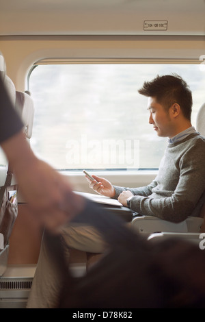 Giovane uomo seduto su un treno usando il suo telefono Foto Stock