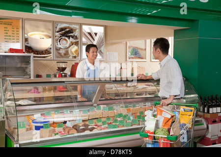 Addetto alle vendite assiste l uomo al contatore Deli, Pechino Foto Stock