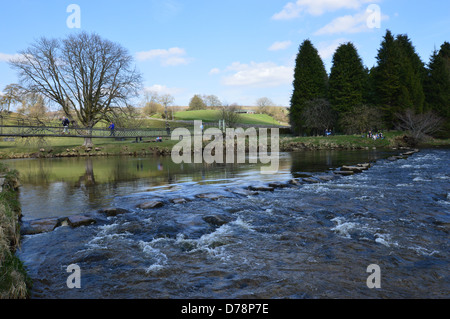 La gente che camminava sul ponte di sospensione & pietre miliari sul fiume Wharfe vicino Hebden sul modo Dales a lunga distanza sentiero Yorkshire Foto Stock