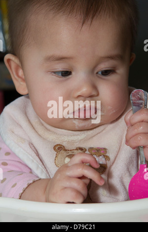 Non impressionati cinque-mese-vecchio baby reagisce al primo cibo solido che tiene il suo cucchiaio di cereali. Foto Stock