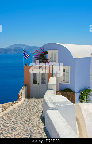 Bella casa con la Grecia bandiera nazionale sulla strada a Santorini, Oia. Mare Egeo in uno sfondo, Grecia Foto Stock