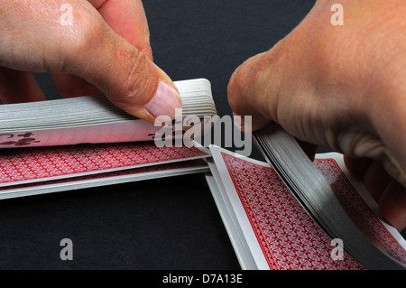 Donna che mischiava un pacco di carte da gioco su uno sfondo nero chiaro. Foto Stock