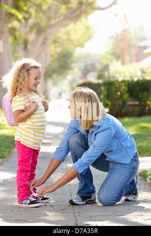 Madre aiutare mia figlia Tie lacci delle scarpe a piedi a scuola Foto Stock