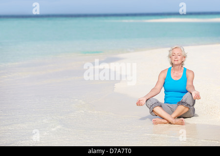 Senior donna meditando sulla bellissima spiaggia Foto Stock