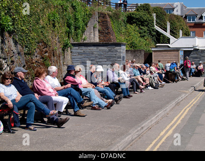 Fila di gente seduta sulle panchine pubbliche, Padstow, Regno Unito 2013 Foto Stock