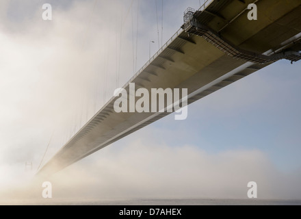 Una sospensione ponte scompare in una fitta nebbia banca su un estuario del fiume. La scarsa visibilità concetto maltempo concettuale Foto Stock