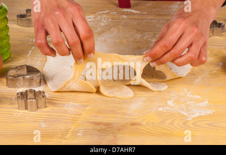 Le mani facendo ritagli di pasta per preparare biscotti fatti in casa Foto Stock