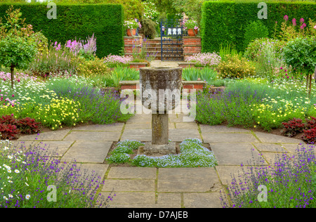 Contrassegnato giardino formale con un vaso di pietra ornamento e fiori d'estate. Foto Stock